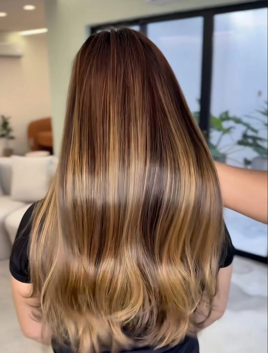 Cabelo longo com mechas iluminadas e finalização lisa, visto de costas no salão