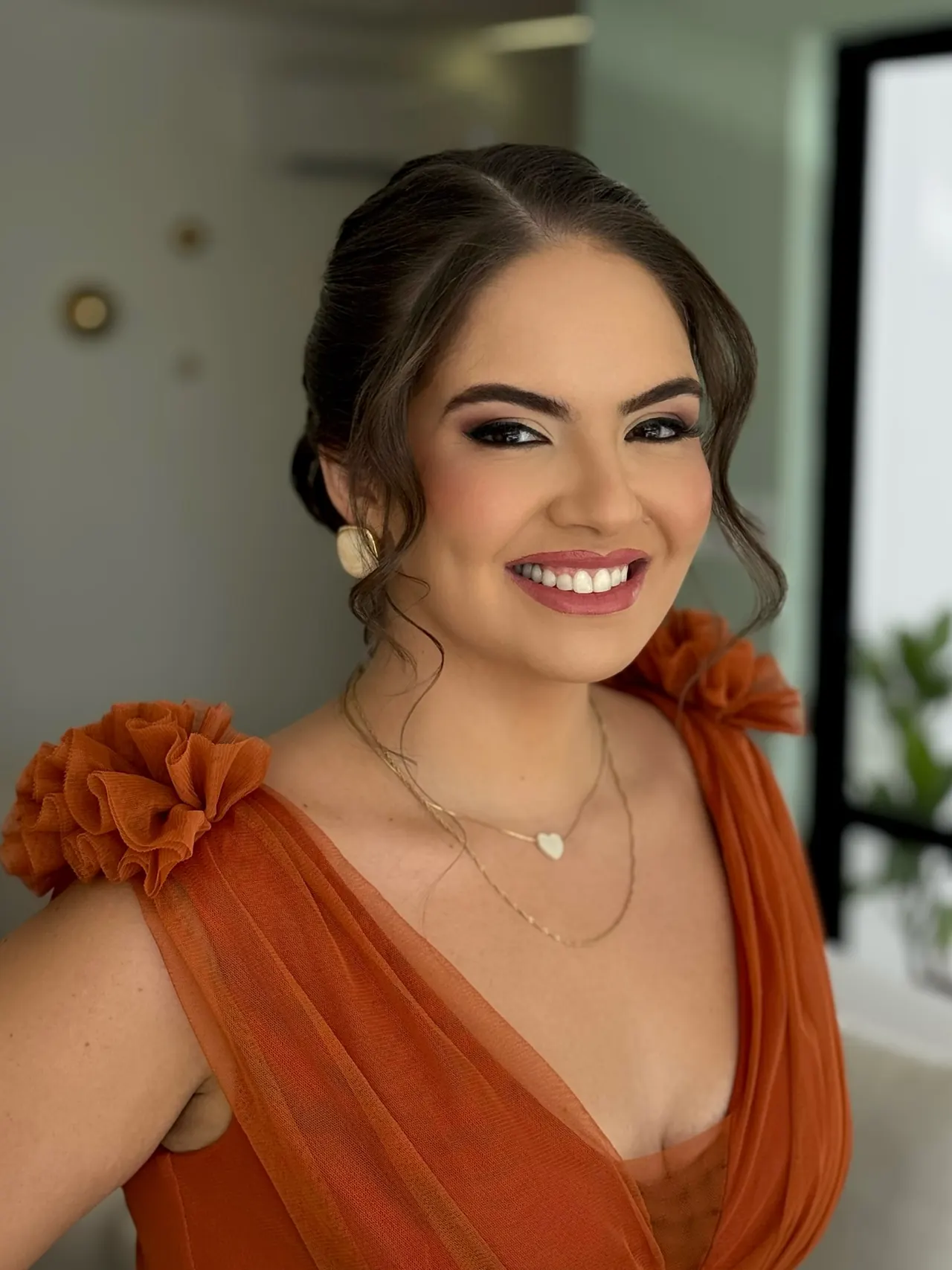 Penteado preso baixo com fios soltos e maquiagem em tons quentes